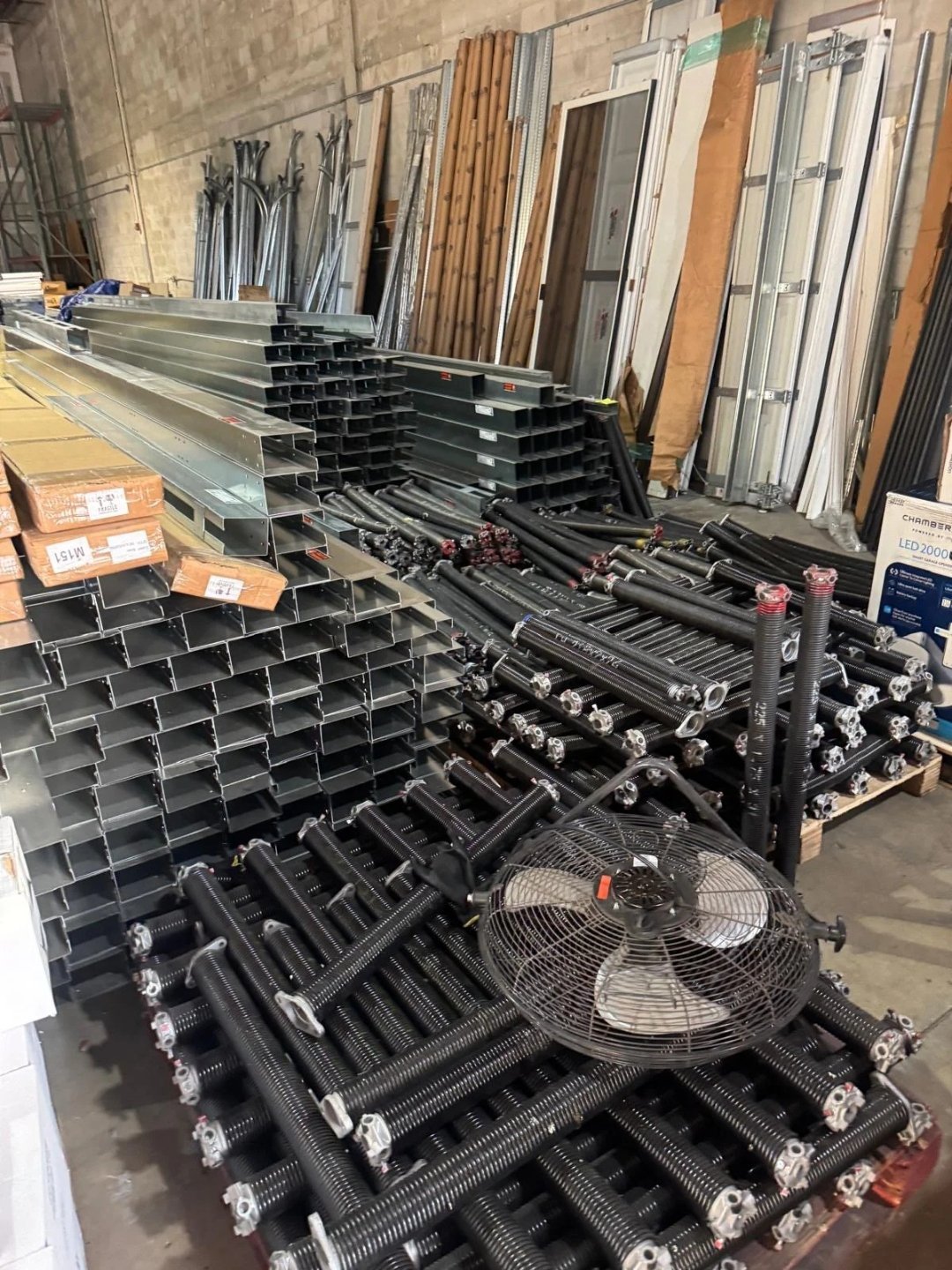 Racks of steel garage door tracks and pallets of black torsion springs in a parts warehouse
