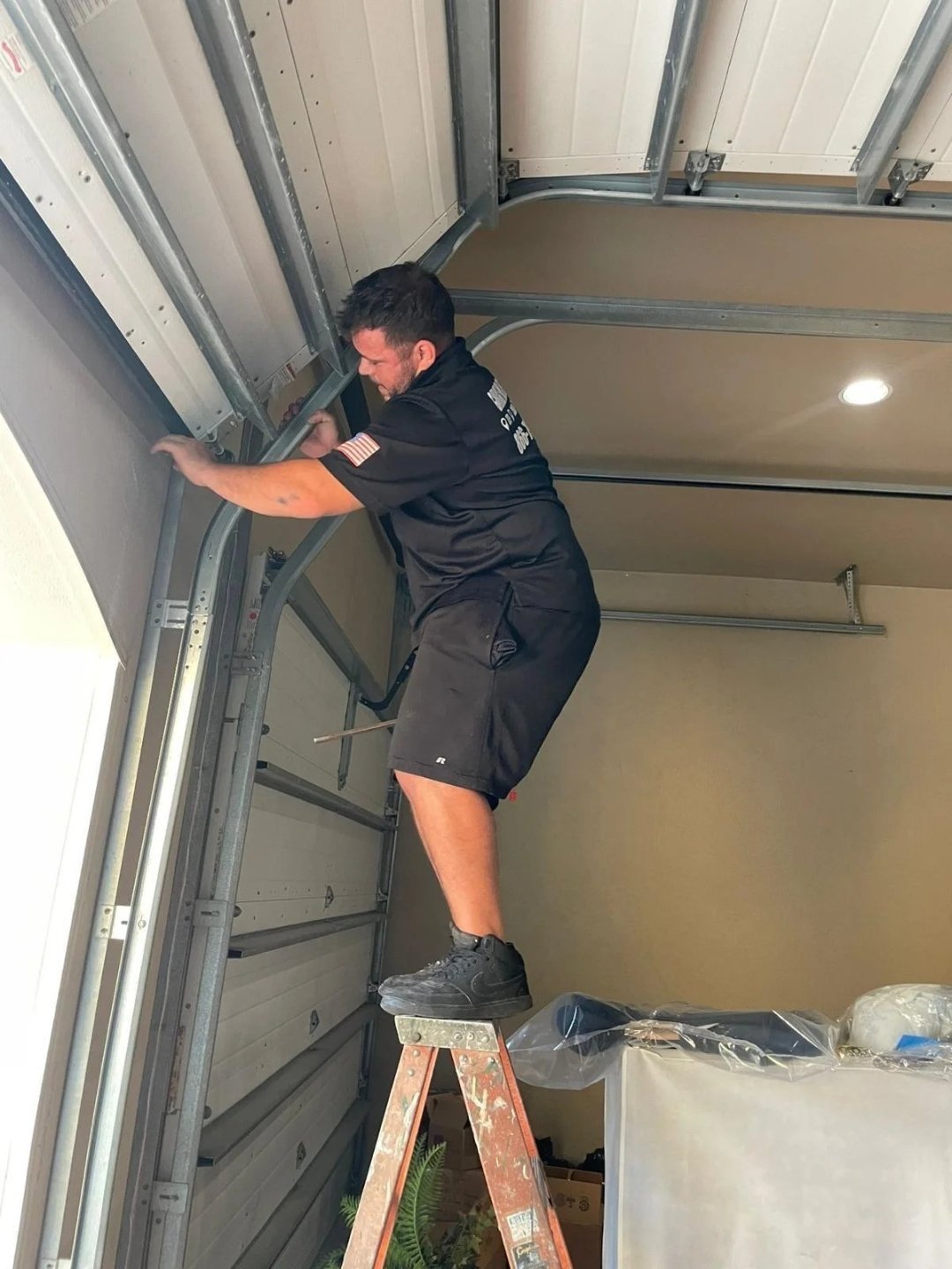 Technician on a stepladder working at the top of a vertical garage door track