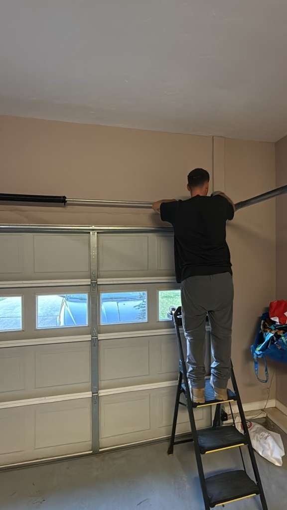 Technician on a stepladder at the top corner of a white sectional garage door
