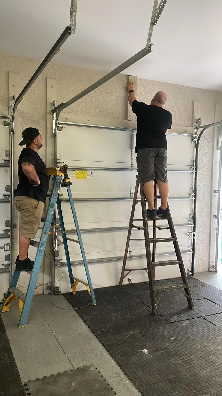 Two technicians on ladders mounting garage door tracks in an empty garage