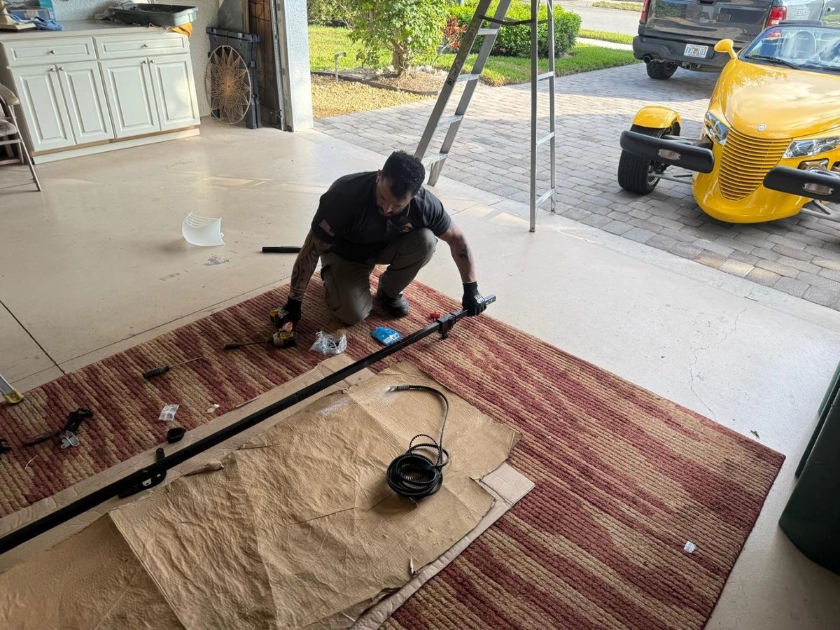 Technician kneeling on a floor mat in an open garage while assembling an opener rail