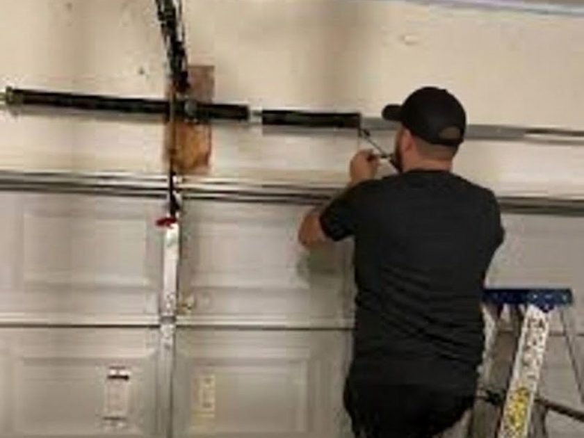 Technician in a cap working on the spring bar above a door