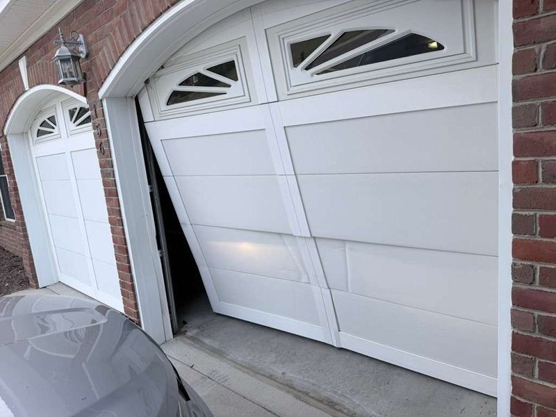 Garage door bowed out of its left-hand track, leaving a gap beside the opening