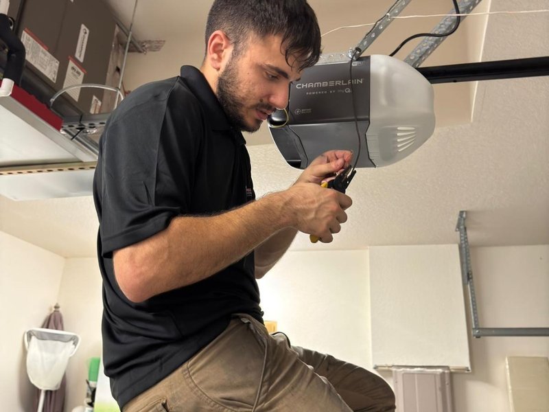Technician on a ladder adjusting a ceiling-mounted opener