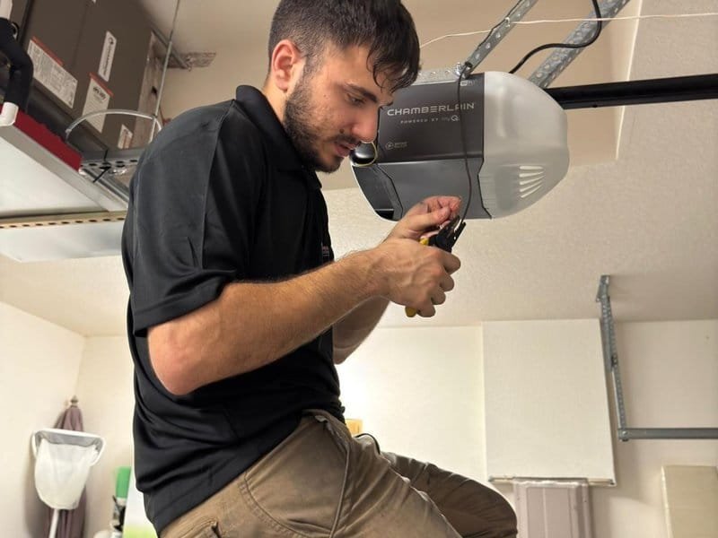 Technician adjusting a ceiling-mounted garage door opener motor unit