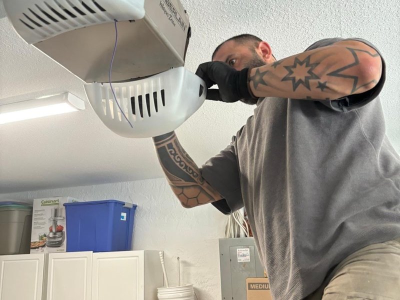 Technician in gloves working on the underside of a ceiling-mounted opener