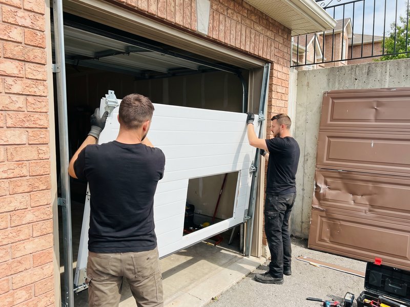 Two technicians lifting a replacement section into a door opening