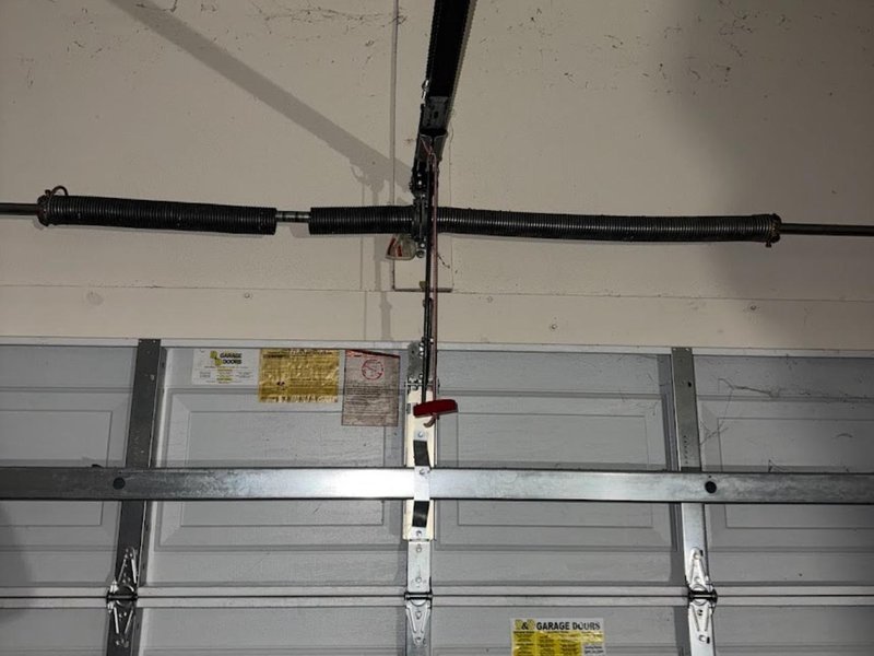 Torsion spring on its bar above the top section of a white door